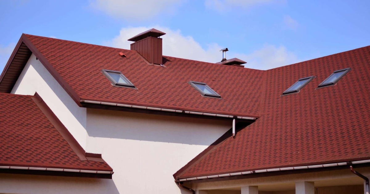 Sunlit shingle roof with skylights under a clear sky